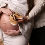 Dłonie rodziców z bucikami na brzuchu ciężarnej kobiety