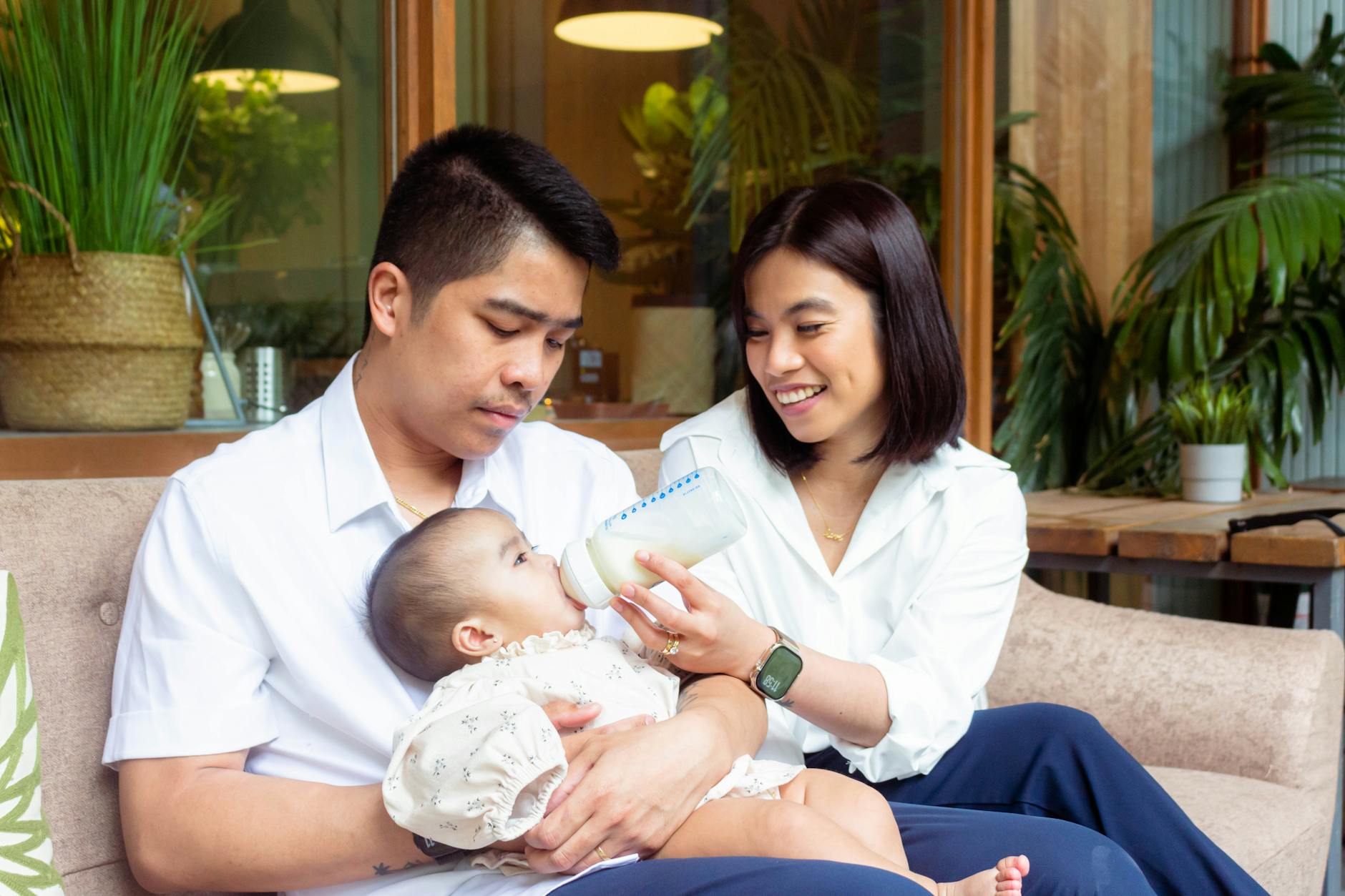 Rodzice karmiący niemowlę butelką w przytulnym, pełnym roślin salonie
