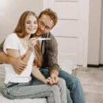 Szczęśliwa para obejmuje się w domu, trzymając pozytywny test ciążowy