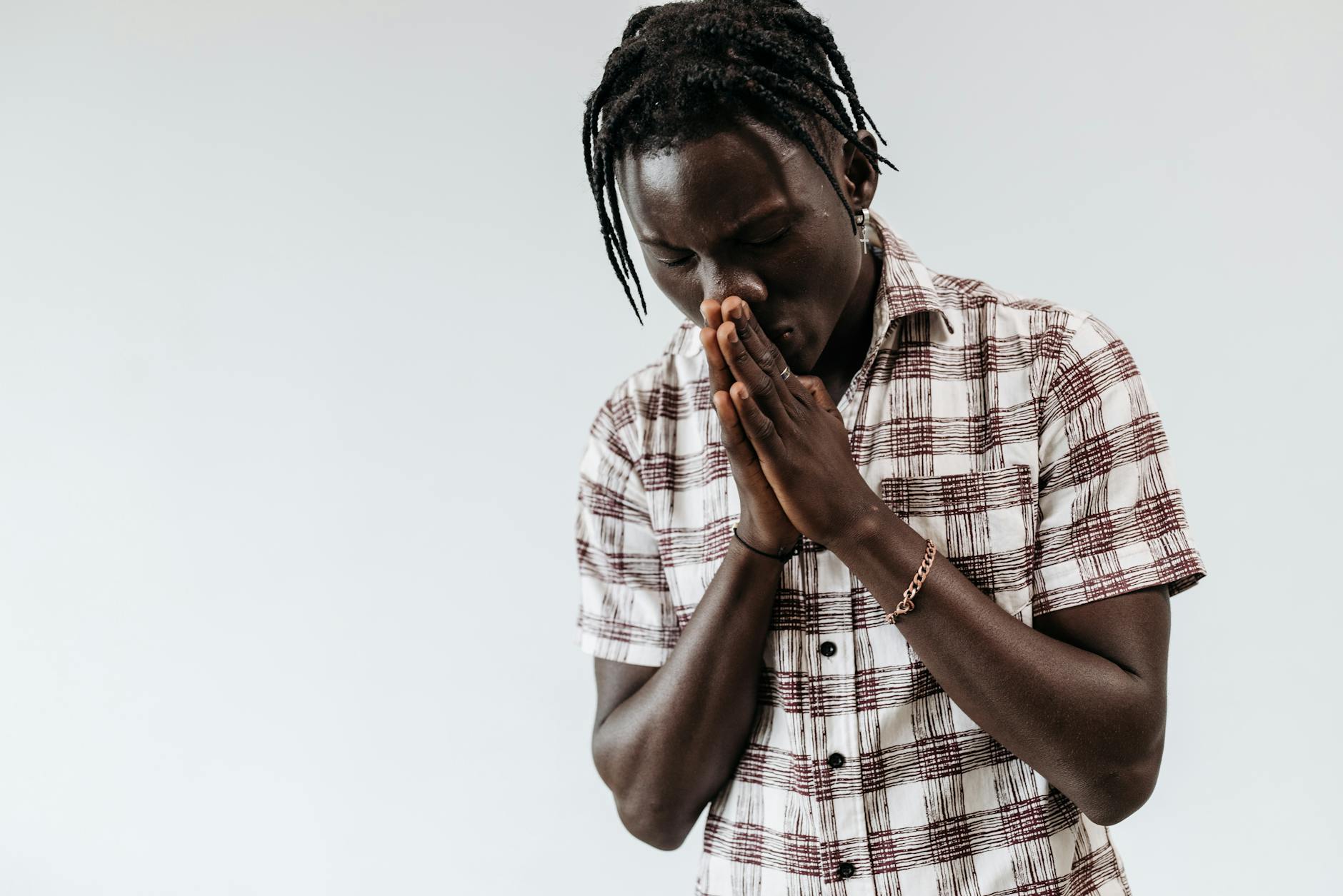 Młody mężczyzna w koszuli w kratę modli się złożonymi dłońmi na białym tle