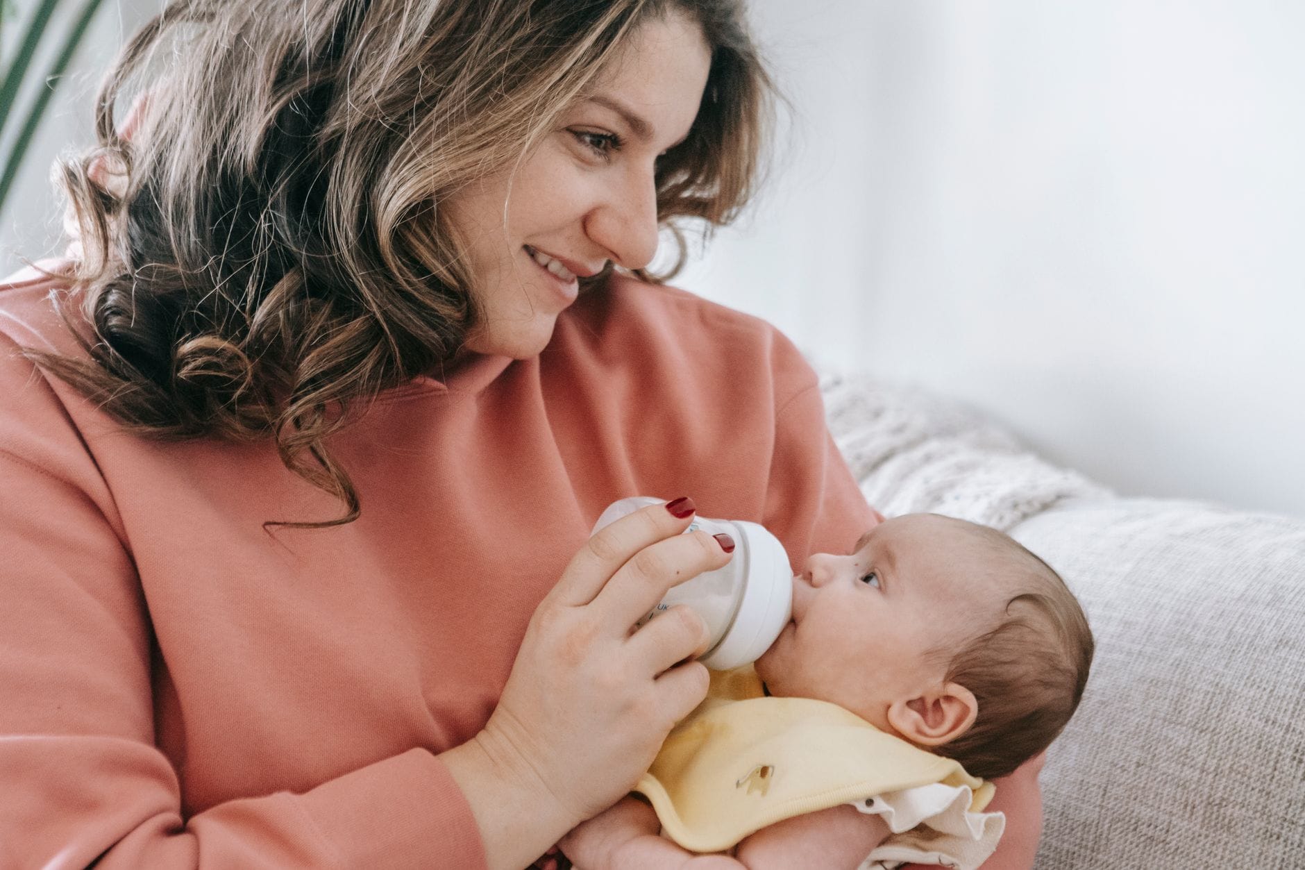 Mama karmi niemowlę butelką na kanapie w jasnym salonie